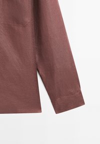 Manche longue d'une chemise rose poudré avec un poignet visible et un tissu tissé texturé sur fond blanc.