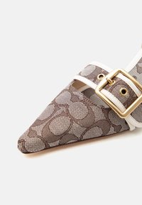 Καφέ παπούτσι με μοτίβο και μυτερή μύτη, με λευκή επένδυση και χρυσή αγκράφα, σε ανοιχτό φόντο.