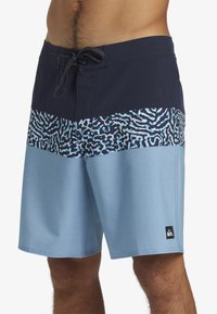 Shorts de bain pour homme avec une ceinture marine, un corps bleu clair et un panneau à motifs vibrants inspirés des coraux dans des nuances de bleu.