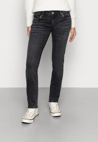 Svarta denimjeans med slim fit, femfickorsdesign och lätt blekning, tillsammans med vita hög-top sneakers.