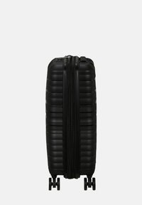 Valigia rigida nera con texture a righe, doppia cerniera e ruote girevoli lisce. Design compatto con dettagli hardware minimi.