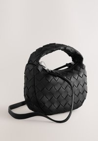 Sac à main en cuir tressé noir avec une forme structurée, une poignée courte et une bandoulière amovible. Comprend une fermeture éclair et des accessoires brillants.