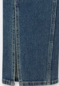 Gros plan sur un tissu en denim bleu avec une fente verticale montrant la doublure intérieure et des coutures détaillées le long des bords.