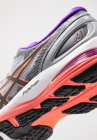 Zapatilla de correr gris con acentos morados, suela de goma negra, marca FlyteFoam y parte superior texturizada. Presenta materiales de malla y sintéticos.