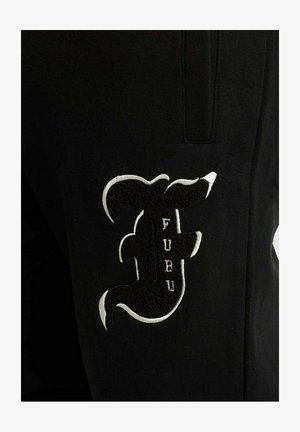 Zwarte stof met een groot geborduurd logo in wit en zwart met de tekst "FUBU" en decoratieve krullen. Close-up weergave.