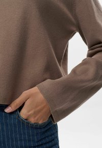Maglione marrone chiaro con colletto a girocollo, polsini a coste e vestibilità comoda. Abbinato a jeans di denim a righe blu scuro.