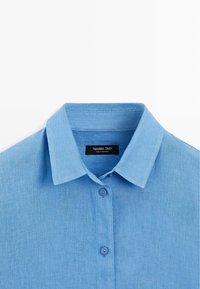 Lyseblå skjorte med knapper foran, spids krave, to synlige knapper og et sort mærke indeni kraven med teksten Massimo Dutti.