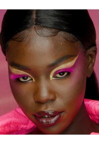 Primo piano di un volto con trucco audace. Ombretto rosa brillante e dorato, eyeliner nero e labbra color borgogna intenso. Texture della pelle liscia, capelli lucenti.