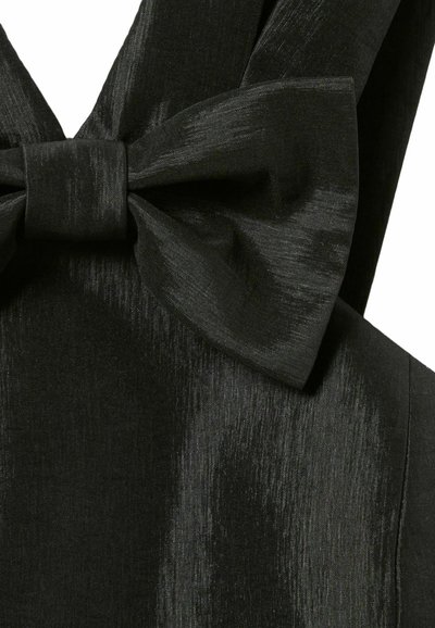 Tessuto nero con una superficie liscia e lucida, caratterizzato da un grande dettaglio a fiocco. Il fiocco è fissato al centro, creando un effetto a strati.