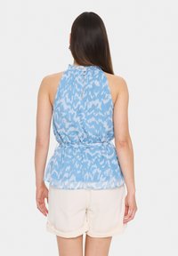 Haut halter bleu à motif avec une coupe ample et un dos en détail en clé, associé à un short couleur crème. Tissu léger et aéré.