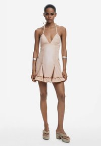 Vestido tipo halter color durazno con escote en V profundo, dobladillo con volantes y aberturas laterales; fabricado con una tela suave y ligera.