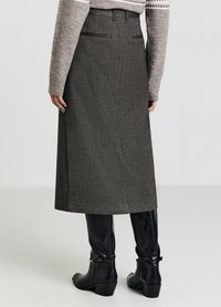 Gonna midi grigia a fantasia con vita alta, tasche laterali e silhouette dritta, abbinata a stivali neri in pelle al ginocchio.