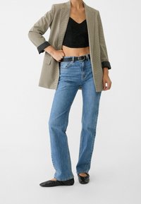 Brun rutigt blazer över en svart spetscroptop, matchat med ljusblå raka jeans och svarta lägenheter. Texturerade tygdetaljer är synliga.