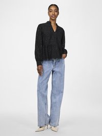 Black embroidered blouse with a scalloped hem, paired with light blue wide-leg jeans and beige pointed heels.