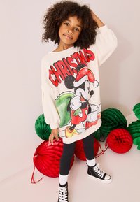 Krämfärgad sweatshirt med en stor Mickey Mouse-grafik i röd och grön för julen. Kombineras med svarta leggins och svarta högskaftade skor.