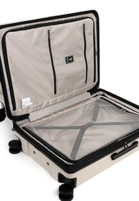Harde beige koffer open om de binnenkant te tonen met een gezeefde compartiment met rits, binnenkant van het deksel met zakken, zwarte handgreep en vier zwarte wielen.