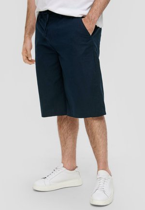 Marineblaue Shorts aus leichtem Stoff, mit lockerer Passform, seitlichen Taschen und geradem Saum; kombiniert mit weißen Turnschuhen.