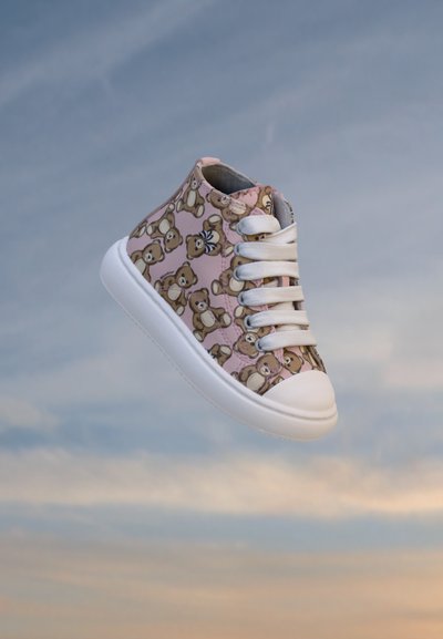 Висок спортен обувка със бяла подметка и връзки, розова материя, покрита с мотиви на плюшени мечета, показана на мек фон на небето.