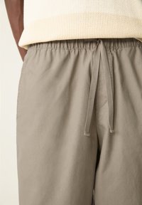 Shorts grii deschis dintr-un material moale și ușor. Prezintă o talie elastică cu șnur și buzunare laterale.