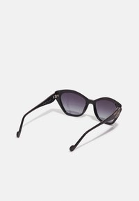 Des lunettes de soleil noires en forme d'œil de chat avec des verres dégradés, une monture en plastique et des accents de quincaillerie dorée sur les branches.