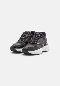 Black and white sneakers featuring a mesh upper, glossy leather accents, chunky sole, and contrasting laces; branded with "KARL" on the tongue.