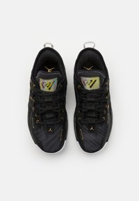 Czarne buty sportowe z siateczkowym wierzchem, złotymi akcentami i kolorowym logo na języku. Charakteryzują się eleganckim designem oraz białą gumową podeszwą.