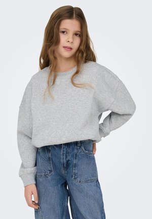 Sudadera gris claro de gran tamaño con hombros caídos y escote redondo, combinada con pantalones vaqueros azules holgados que tienen grandes bolsillos.