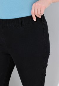 Černé elastické džíny s úzkým střihem, s měkkým pasem a bočními kapsami, zobrazené na neutrálním pozadí.