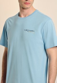 Camiseta de manga corta azul claro hecha de suave tela de algodón, con un pequeño diseño de logo en la zona del pecho.