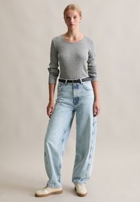 Grey ribbed long-sleeve top paired with light blue baggy jeans and beige sneakers. Includes a black belt and subtle design details.