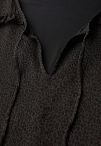 Blusa de estampado de leopardo con una base marrón oscuro y manchas negras, que presenta un escote en forma de V y una tela texturizada.
