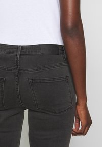 Mustat farkut, joissa on istuva muotoilu, mustalla nahkalla valmistettu etiketti vyötäröllä ja kaksi takataskua. Teksturoitu kangas, sileä pinta.