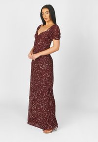 Burgundy iltapuku, jossa on syvä V-pääntie, puffihihat ja siroissa kankaissa harvakseltaan glitteriä, viimeistelty lantioon asti yltävällä siluetilla.