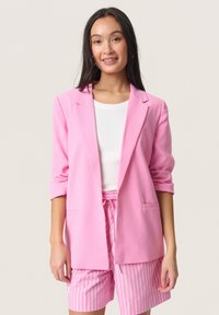 Rosa Blazer aus leichtem Material mit Reverskragen, aufgerollten Ärmeln und zwei vorderen Taschen, kombiniert mit hell gestreiften Shorts.