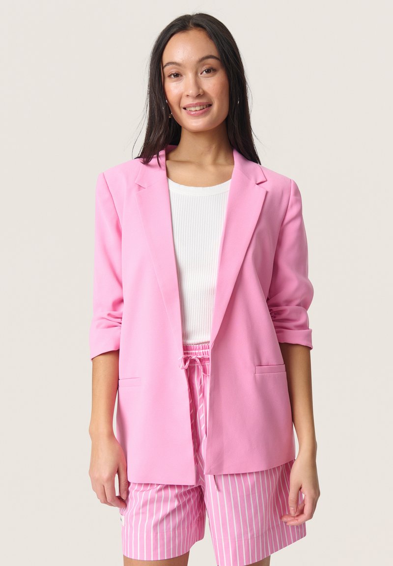 Blazer rose en tissu léger avec un col cranté, des manches retroussées et deux poches avant, associé à un short à rayures légères.