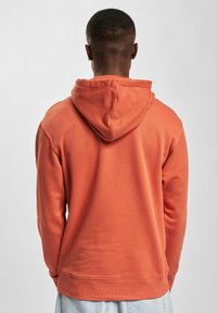 Kapuzensweatshirt in einem gedämpften Orangeton, aus strukturiertem Stoff mit einer Kängurutasche sowie gerippten Bündchen und Saum.