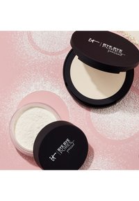 Presse- og løspudder med svarte lokk merket "Bye Bye Pores" på en rosa overflate støvet med hvitt pudder.