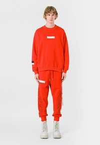 Sudadera roja y joggers a juego de algodón, con un bolsillo delantero y flecos decorativos. Combinado con botas blancas hasta el tobillo.