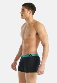 Černé boxerky s petrolejově modrým pasem zdobeným černými pruhy. Tkanina působí hladce a pružně, navržena pro pohodlné nošení.