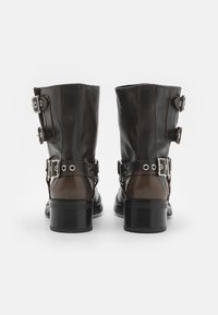 Brune lær ankle boots med en glans finish, prydet med to metal spænder og en kraftig hæl. Glat tekstur og struktureret form.
