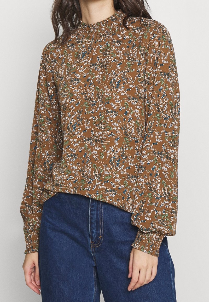Brown floral blouse with long sleeves, gathered neckline, and elastic cuffs. Features white and green patterns with blue accents.