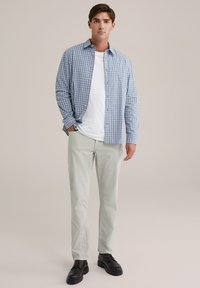 Herrenhemd in Blau- und Weißkaros mit langen Ärmeln, kombiniert mit hellgrauen Hosen und schwarzen Schuhen. Darunter ein schlichtes weißes T-Shirt.