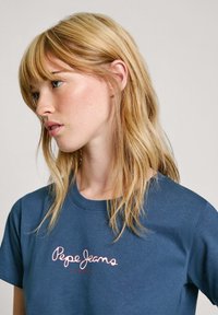 Mėlynas medvilninis marškinėliai su apvaliu kaklu, su rožiniu "Pepe Jeans London" logotipo siuvinėjimu ant krūtinės. Minkšta tekstūra ir atsipalaidavęs siluetas.
