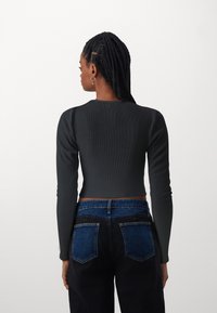 Tumehall ribatud pikakäistega lühike crop top, mis on kombineeritud kõrge vöökohaga mustade pükstega, mille seljataskutel on sinised denimäärised.