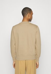 Felpa beige con collo a giro e maniche lunghe, polsini e orlo a coste. Tessuto morbido con vestibilità comoda, indossata con pantaloni abbinati.