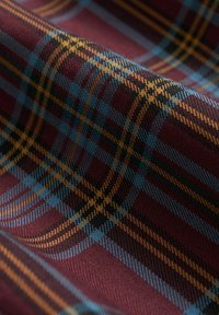 Tartan-Stoff mit einem tiefen burgunderfarbenen Hintergrund, auf dem blaue, gelbe und schwarze Linien ein Rautenmuster bilden. Weiche, strukturierte Oberfläche.