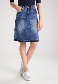 Világoskék farmer szoknya, enyhe kopással, közép hosszúságú, rojtos szegéllyel, elöl gombos záródással és két oldalsó zsebből áll.