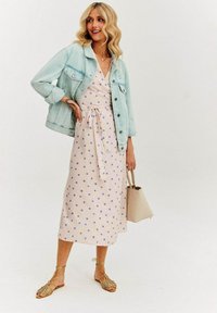 Jasnoniebieska kurtka dżinsowa nałożona na sukienkę w kropki w miękkim różu z niebieskimi kropkami. Uzupełniona beżową torebką i płaskimi sandałkami na paski.