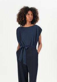 Jumpsuit blu navy con una vestibilità comoda, scollo rotondo e maniche corte. Presenta una cintura in vita e tasche laterali. Tessuto dalla trama liscia.