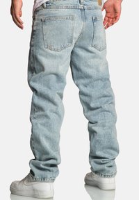 Jasnoniebieskie dżinsy o luźnym kroju, widoczne przeszycia, dwie tylne kieszenie oraz przetarty materiał. W zestawie białe trampki.